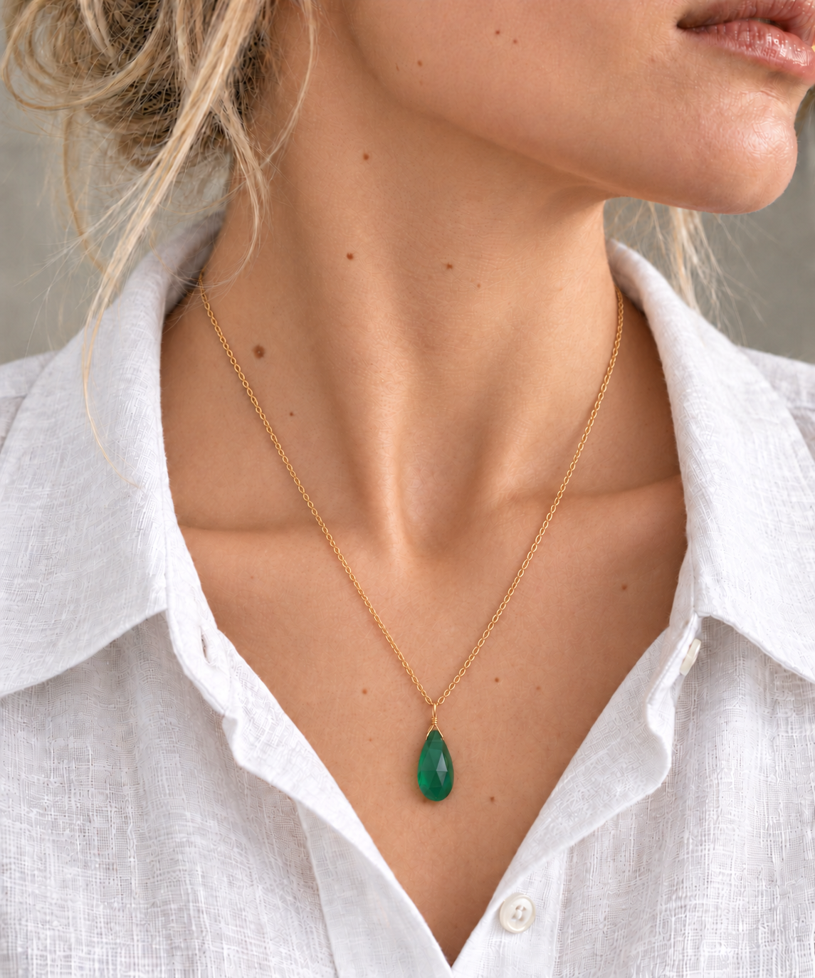Green onyx teardrop pendant necklace on a model wearing an open-collar white shirt.